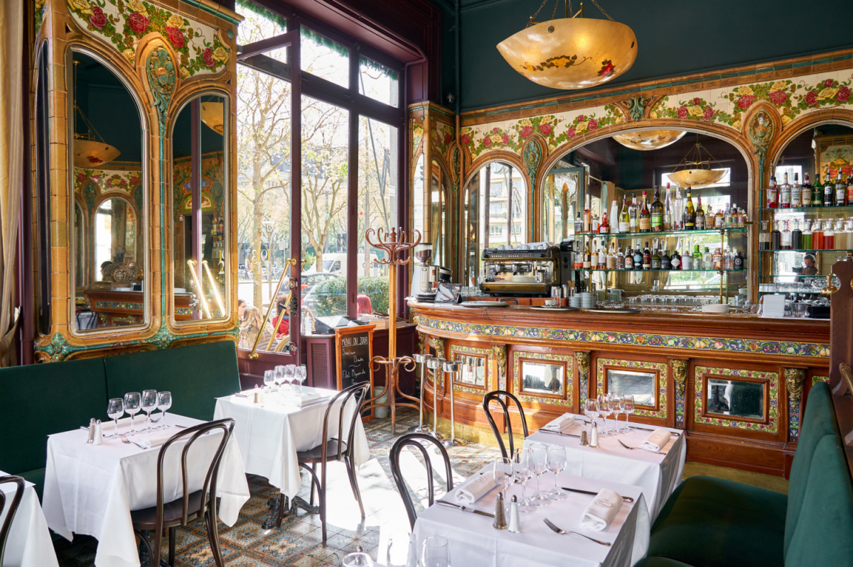 Salle de brasserie aux boiseries et faïences décorées, tables dressées en nappes blanches