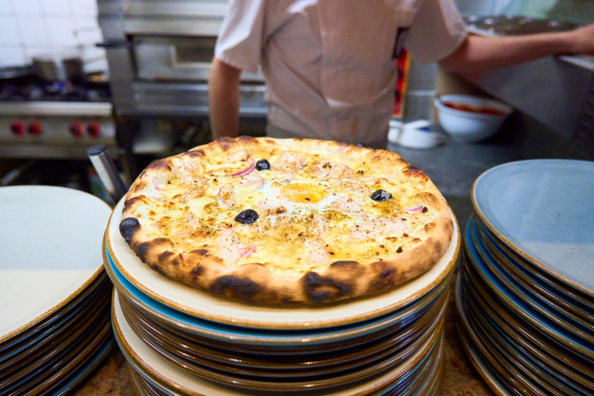 Pizza dorée posée sur une pile d'assiettes, au poste du pizzaiolo